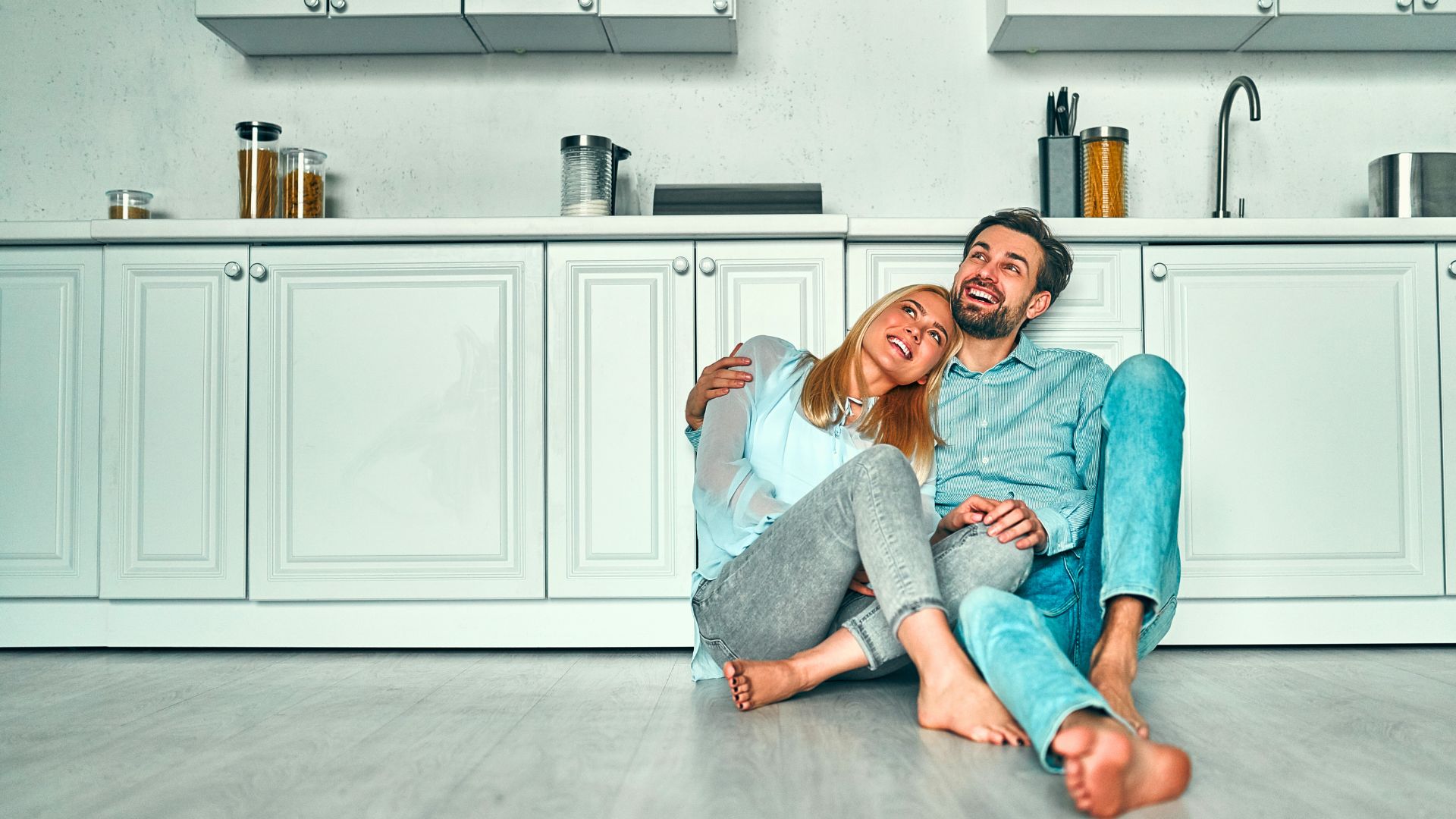 a happy couple sits on the floor and leans against their new cabinets