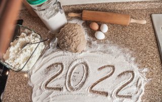 New Year in the kitchen. 2022 is written in flour. A piece of dough, eggs and a wooden rolling pin lies on a granite countertop